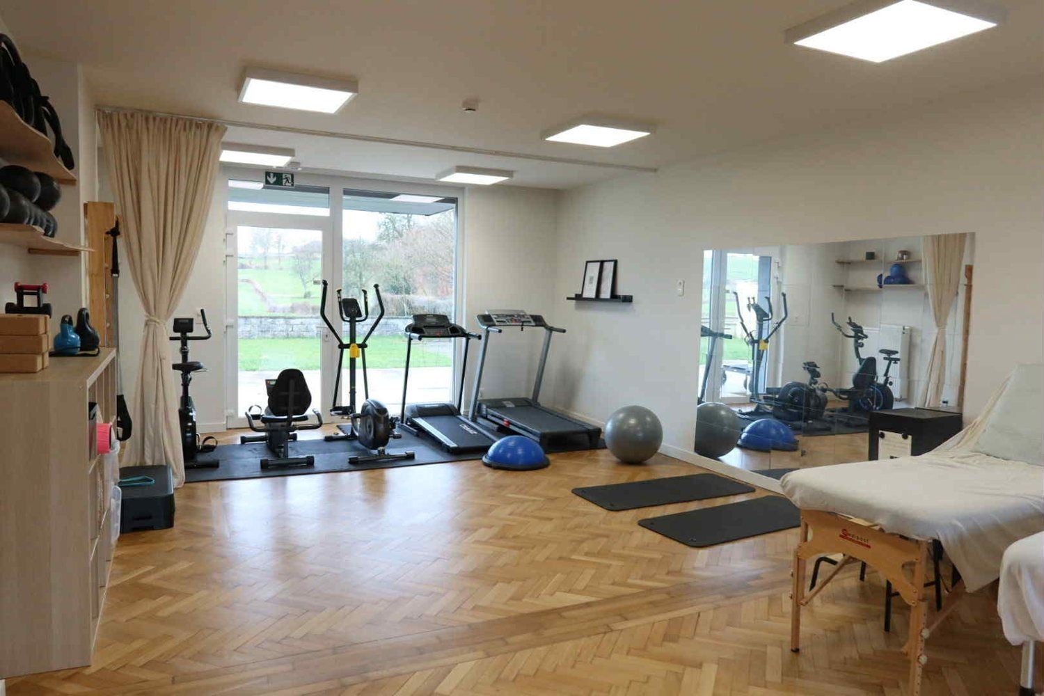 La salle de rééducation : parquet en chevrons, vélo, tapis de course, table de soin